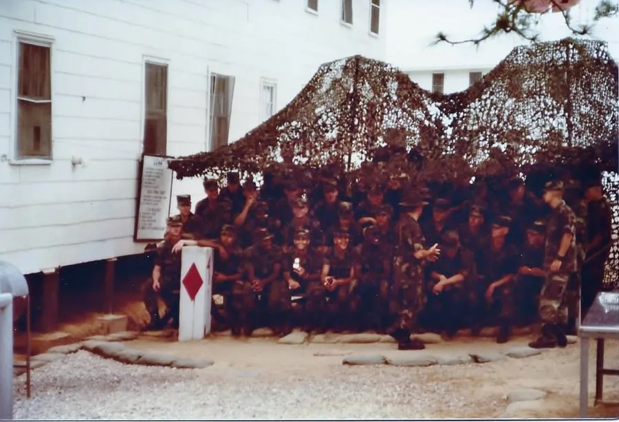 Basic training platoon under the camouflage net — Alex holding the award