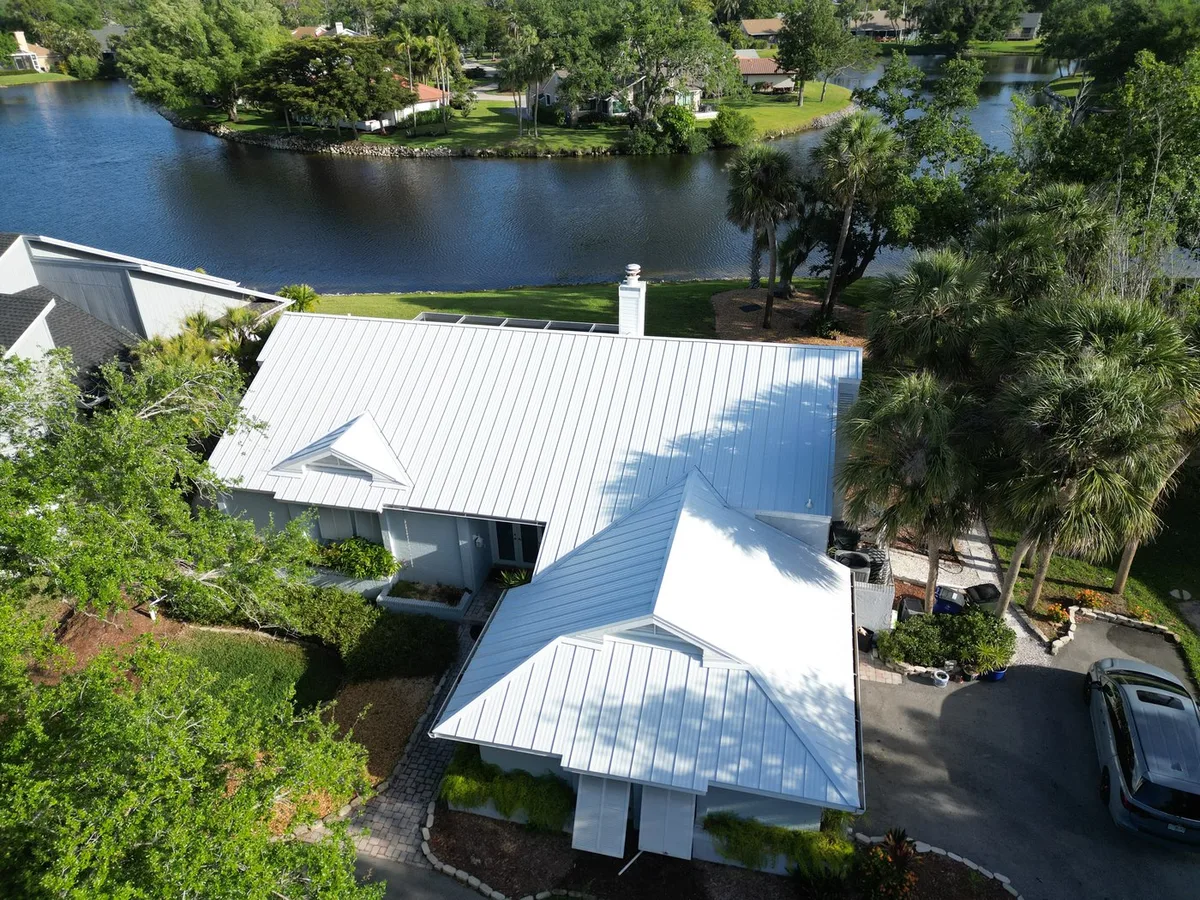 White standing-seam metal roof on a waterfront home — aerial