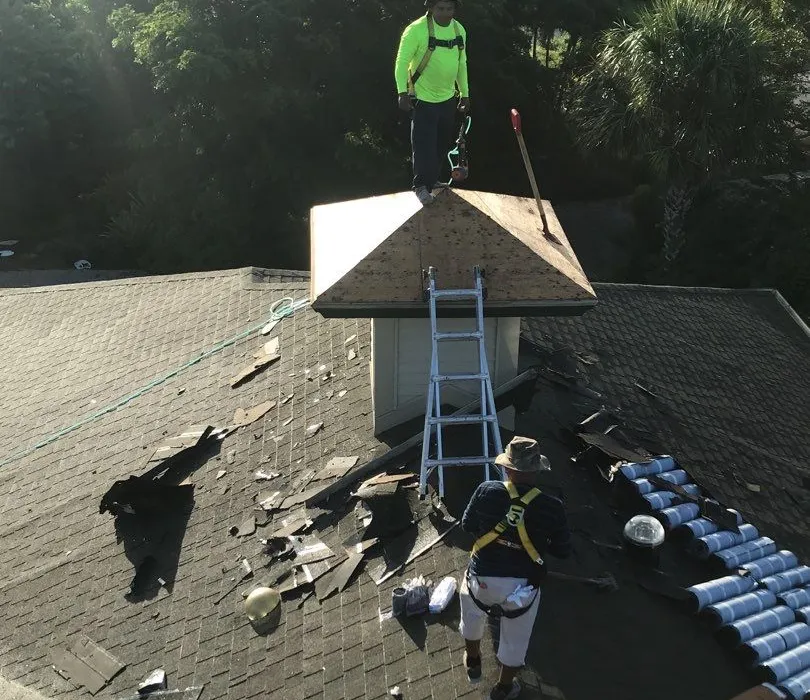 Blue Dog crew in harnesses tearing off the same Sanibel roof, new tile staged on the deck