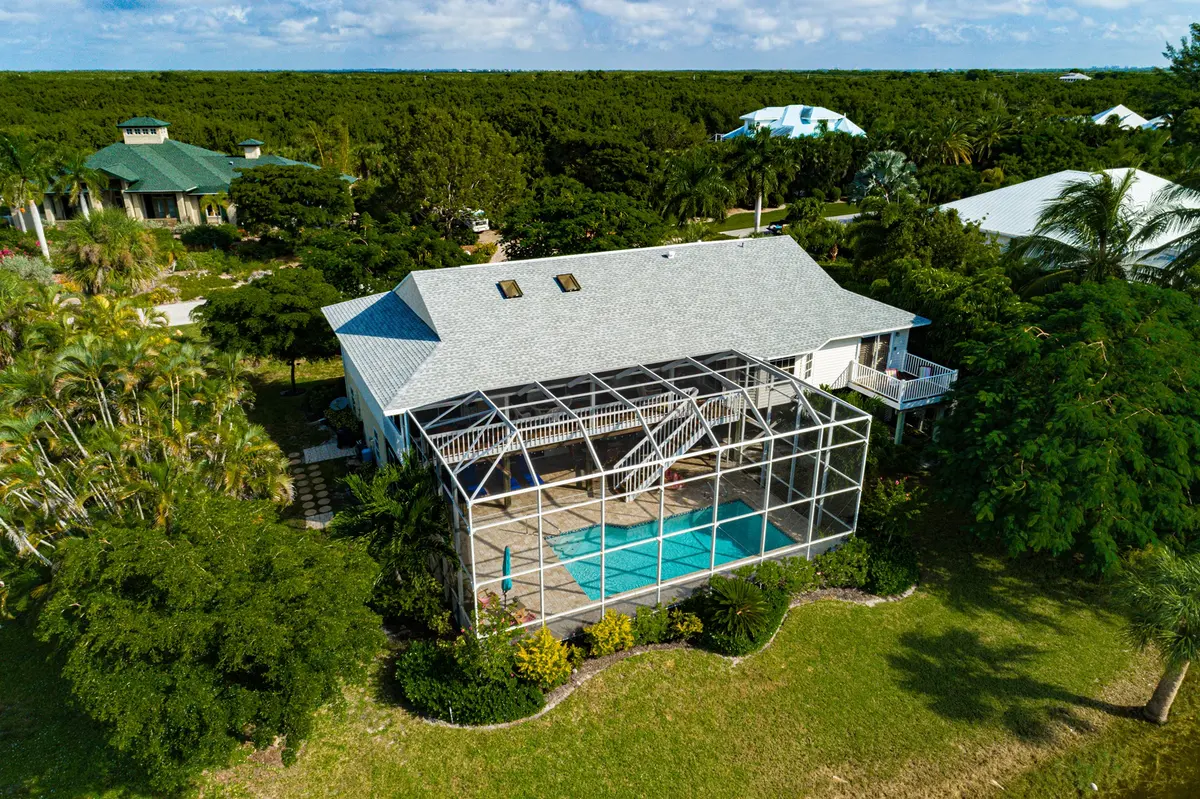 Sanibel pool home with a new gray shingle roof, and the green-roofed neighbor behind it — both Blue Dog roofs